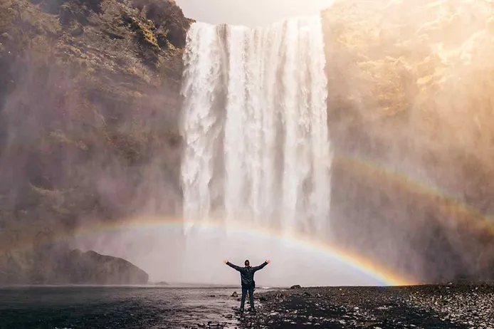 Iceland's warterfall, skogafoss, with a rainbow and a tourist enjoying the mist