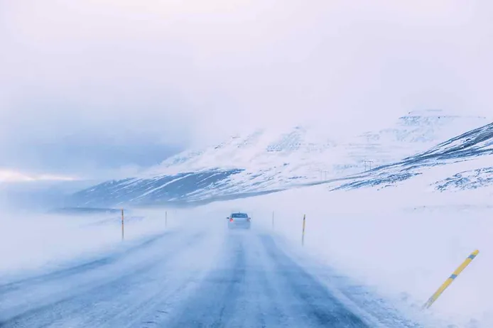 Car driving on a foggy road in a very snow covered area