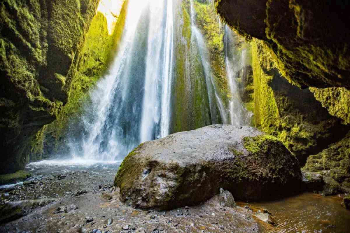 A stunning waterfall cascades into a calm pool, surrounded by moss-covered rocks and lush vegetation in Nauthúsagil Ravine, Iceland, showcasing the natural beauty and serenity of the area.