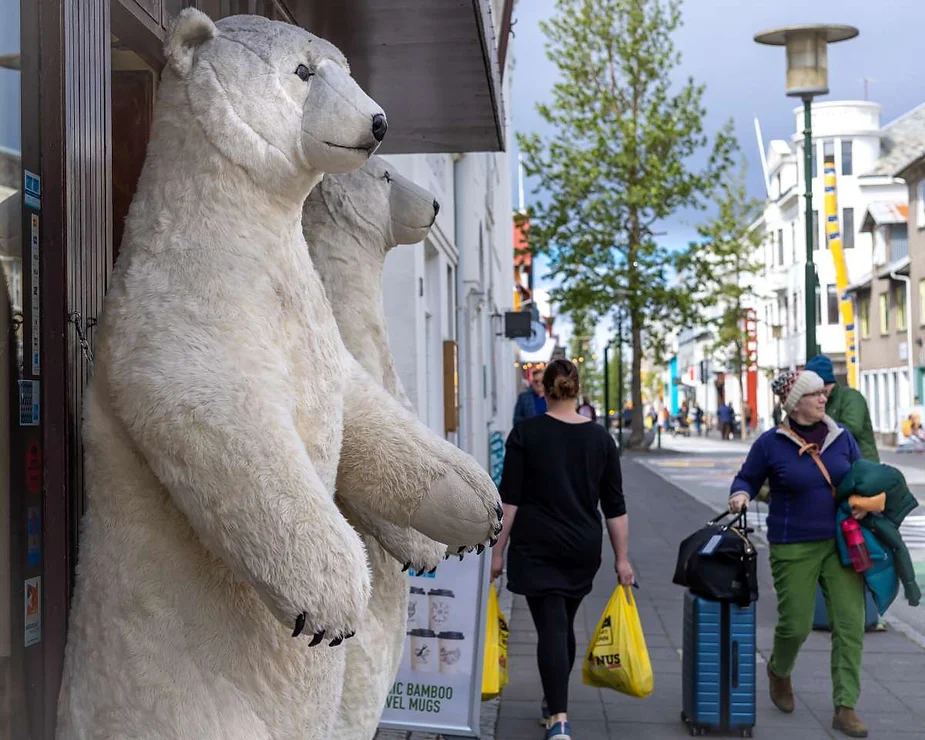 Large polar bear statues stand at the entrance of a shop on a bustling street, with pedestrians walking by and carrying shopping bags.