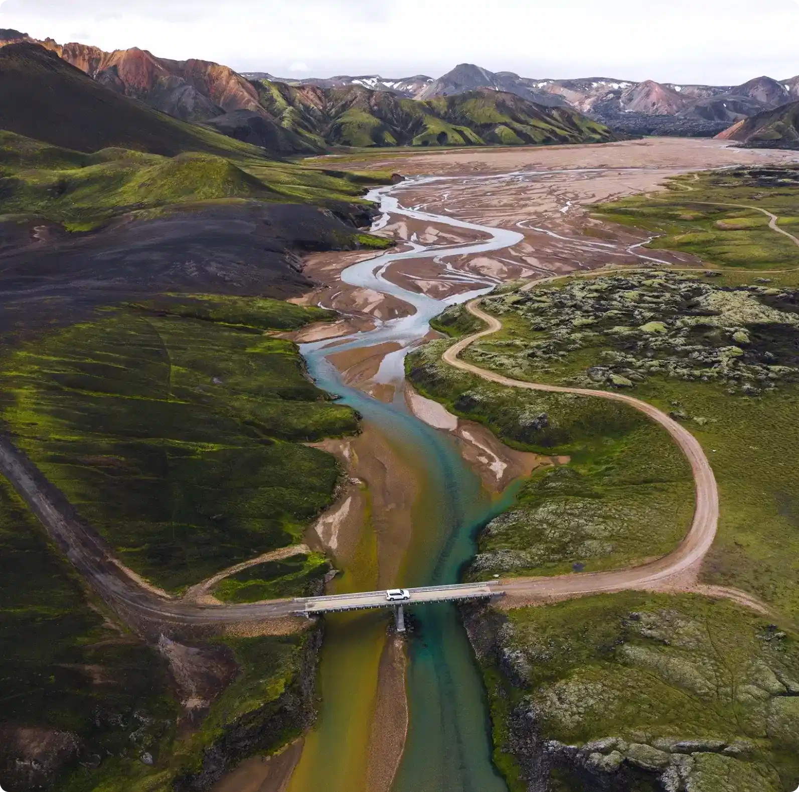 Aerial view of a winding river and rugged Icelandic highlands with a car crossing a bridge, symbolizing the adventure and freedom of exploring Iceland with a rental car.