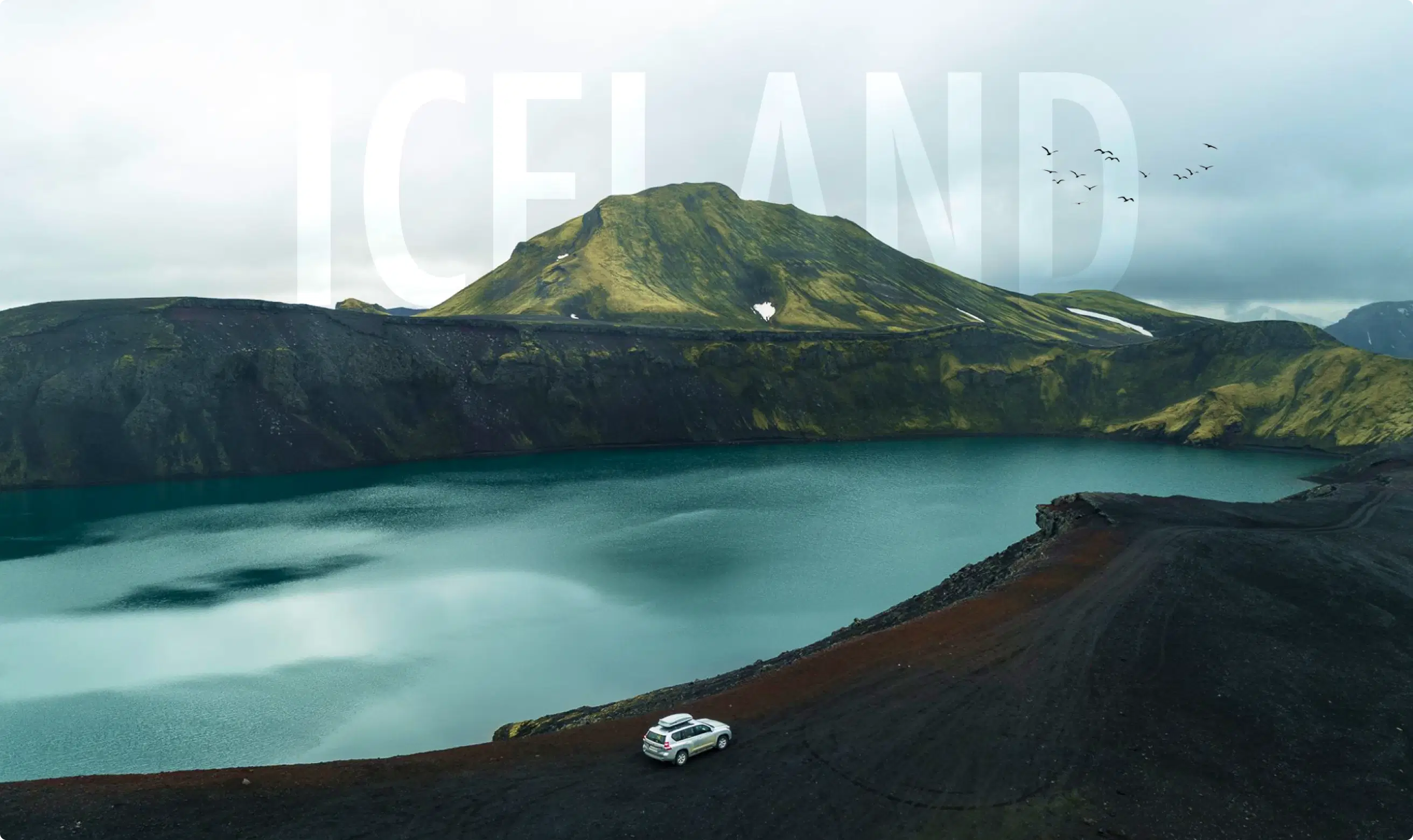 Scenic view of a car parked near a crater lake surrounded by rugged mountains in Iceland, with large 'ICELAND' text overlaying the sky.