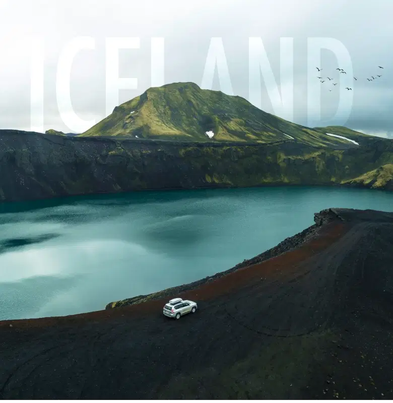 Scenic view of a car parked near a crater lake surrounded by rugged mountains in Iceland, with large 'ICELAND' text overlaying the sky.