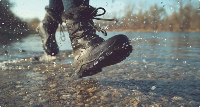 Nahaufnahme von wasserdichten Wanderschuhen, die in einem flachen Bach spritzen, ideal für die Erkundung der feuchten und unebenen Gelände in Island.