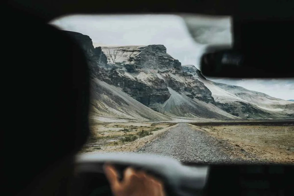 Blick aus dem Auto auf einen steinigen Schotterweg, der zu bergigen Klippen in Island führt.