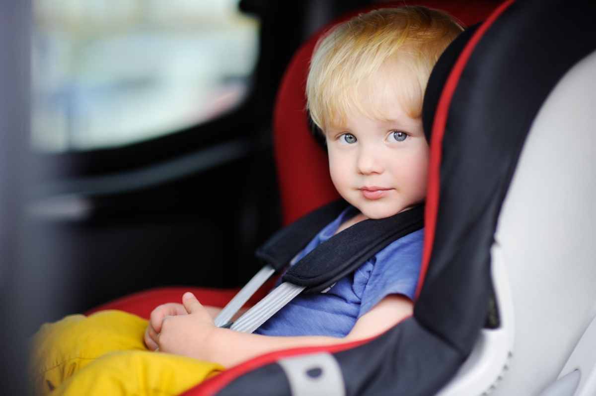 Blonder Junge mit blauen Augen, der in seinem Kindersitz in einem Mietwagen angeschnallt ist