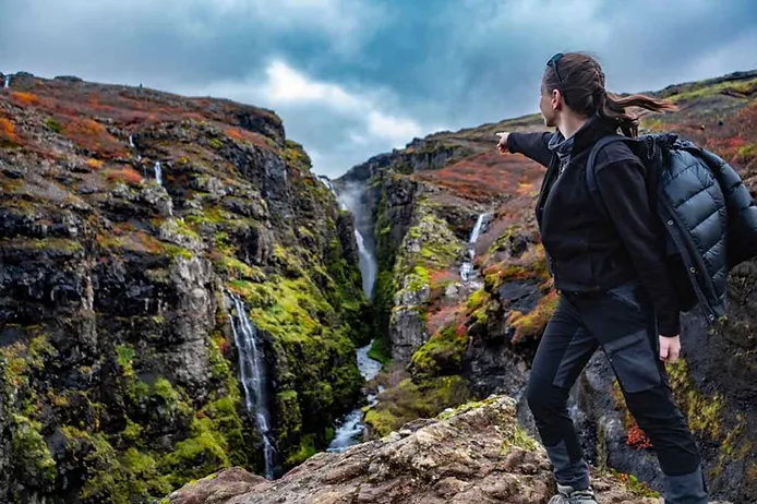 Wanderer, der auf den Glymur-Wasserfall in Island zeigt