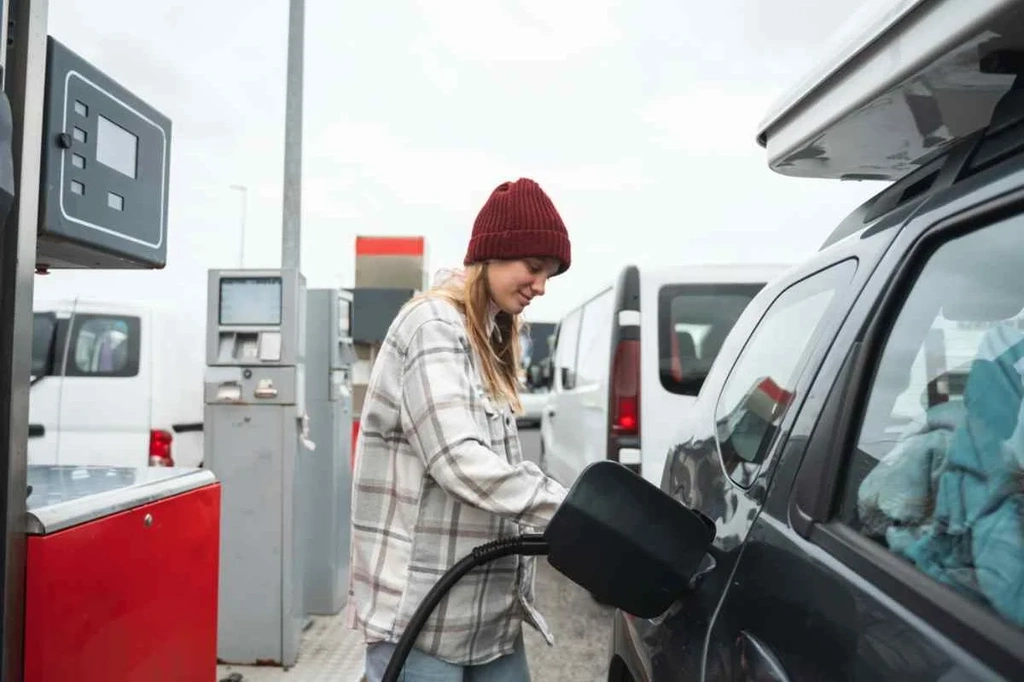 Eine Frau mit roter Mütze und kariertem Hemd tankt ihr Fahrzeug an einer isländischen Tankstelle auf.