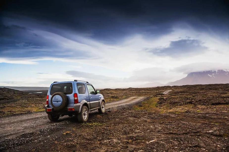 SUV azul en un camino de tierra áspero en islandia con cielos dramáticos y un paisaje volcánico al fondo capturando el espíritu de la aventura