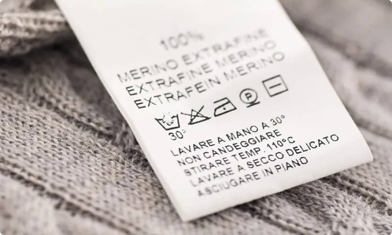 Gros plan sur l'étiquette d'entretien d'un vêtement en laine mérinos, indiquant les instructions de lavage et de séchage pour les couches de base en Islande.