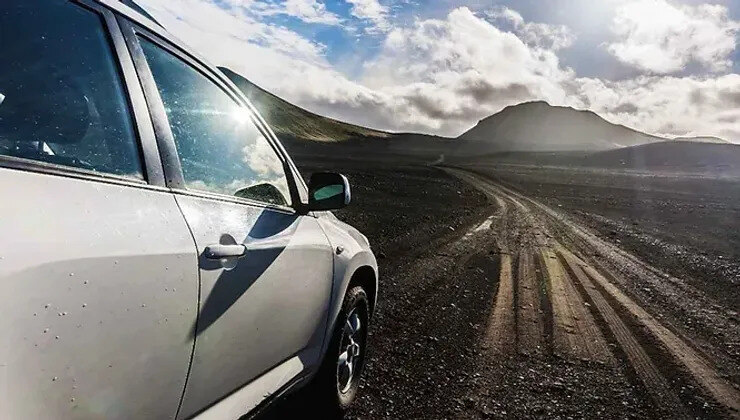 Un SUV blanc garé sur une route de gravier dans les étendues sauvages d'Islande avec des montagnes escarpées en arrière-plan.