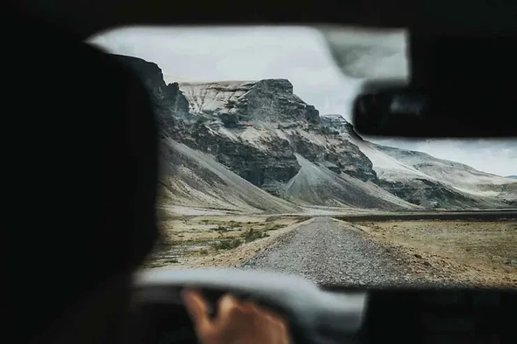 Vue depuis un conducteur sur un chemin de gravier rocheux menant à des falaises montagneuses en Islande.