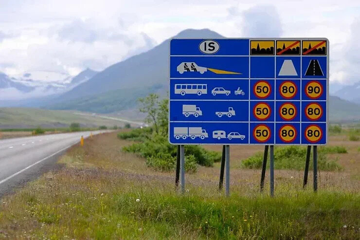 Panneau routier en Islande affichant diverses limites de vitesse selon les types de véhicules, avec un paysage montagneux en arrière-plan.