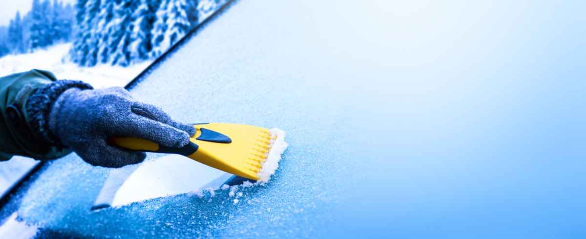 Conducteur grattant un pare-brise recouvert de glace avec un grattoir