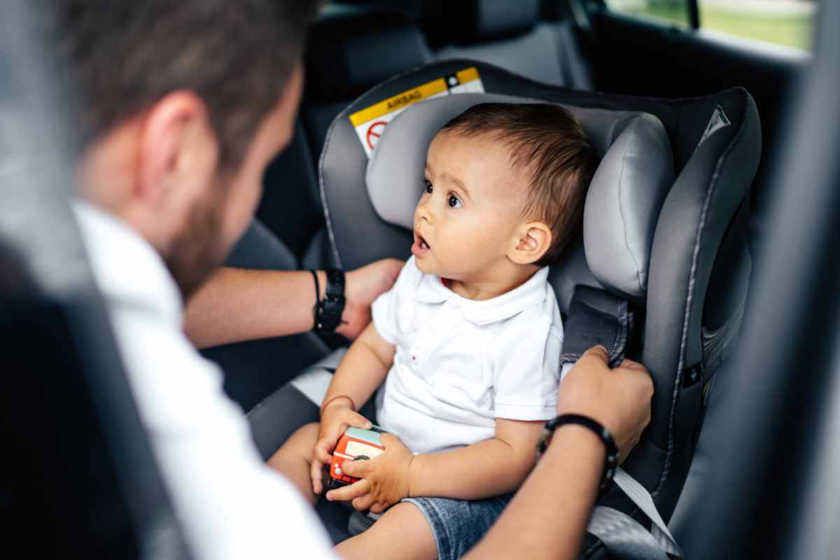 Papà che allaccia un adorabile bambino al suo seggiolino auto